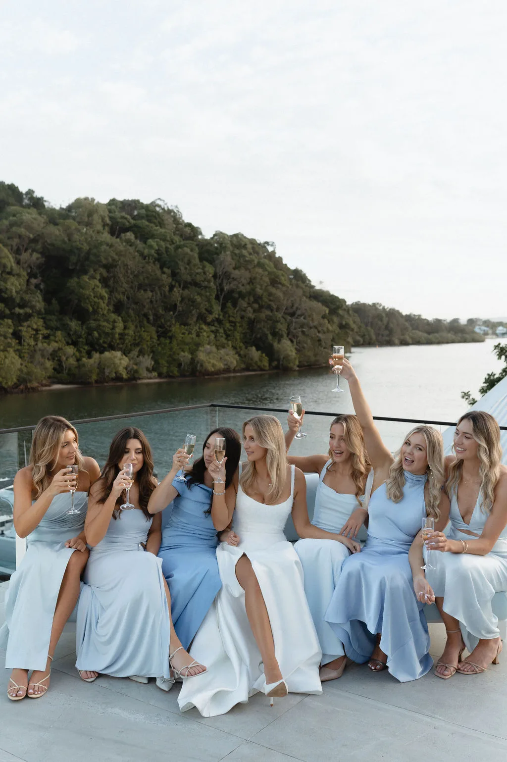 Bridesmaids seated on the terrace, raised glasses over the river