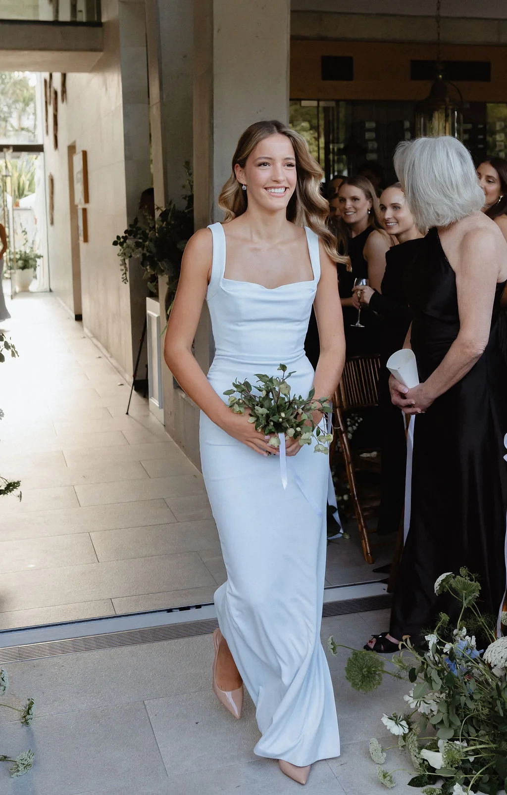 Bridesmaid walking to the ceremony with guests looking on